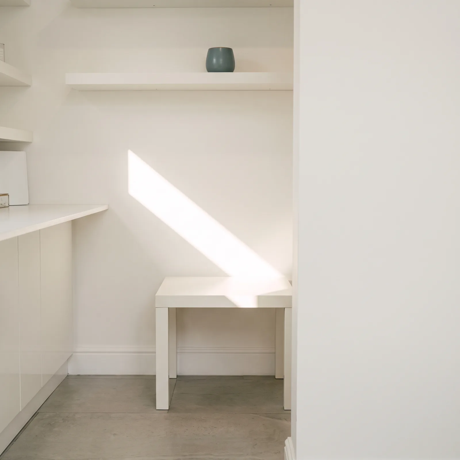 A single stripe of window light across the wall and the empty table